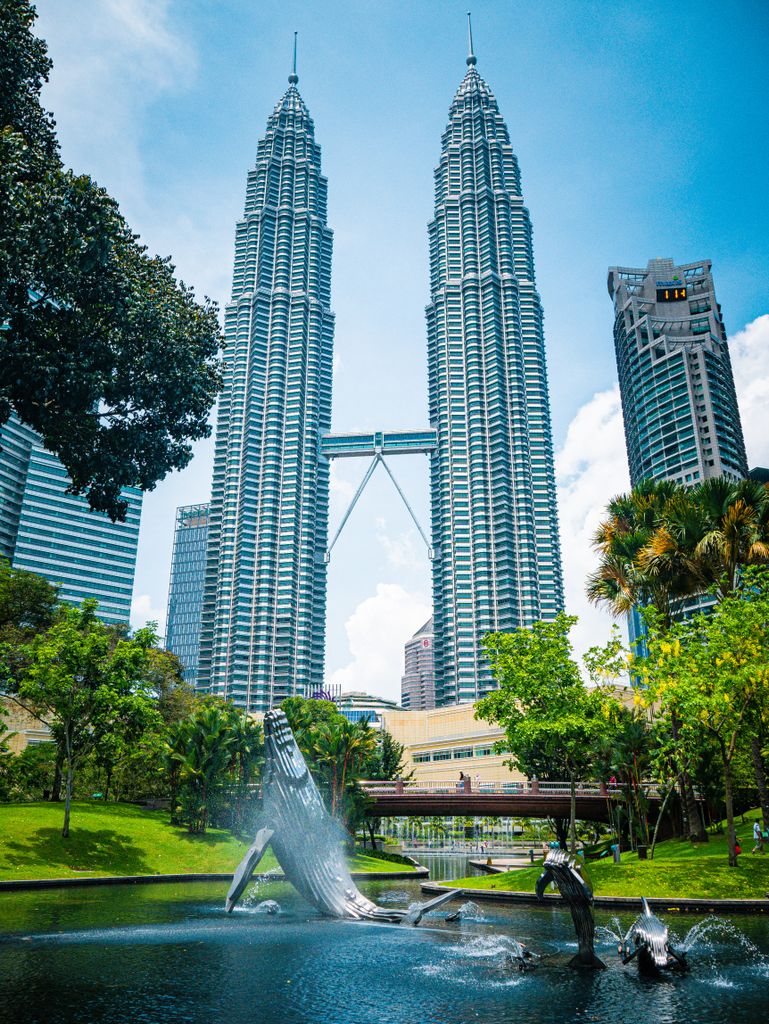 View of Petronas Twin Towers and surrounding park in Kuala Lumpur under a blue sky.